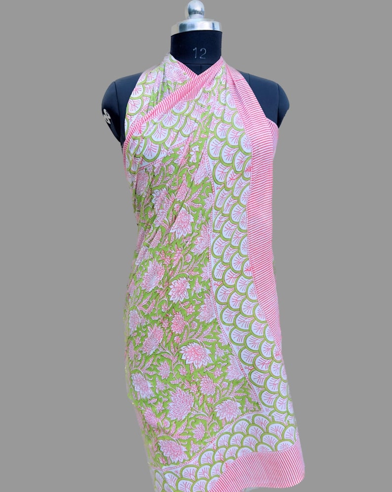 Puede incluir: Un pareo con estampado floral verde y rosa exhibido en un maniqu&iacute;. El pareo presenta un gran estampado floral en un lado y un borde a rayas en el otro. La tela est&aacute; drapeada para mostrar el dise&ntilde;o.
