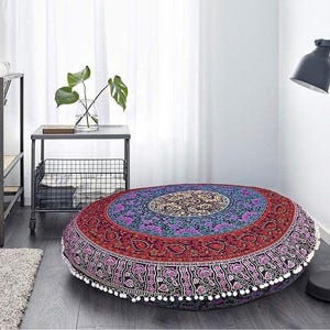 May include: A large, round floor cushion with a vibrant mandala design. The cushion features a central medallion in gold, surrounded by concentric rings of red, purple, and blue. White pom-poms trim the edge. This decorative cushion is perfect for a living room or meditation space.