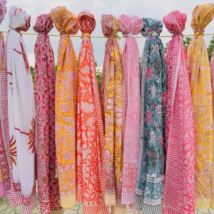 Peut inclure: Une collection de 10 écharpes en coton colorées avec des motifs floraux et géométriques. Les écharpes sont suspendues à une corde à linge et sont toutes de couleurs et de motifs différents.