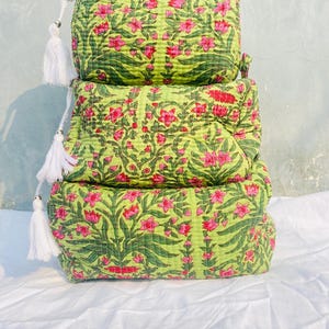 Op de afbeelding: Drie groene en roze bedrukte, gestikte stoffen zakjes met witte kwastjes.