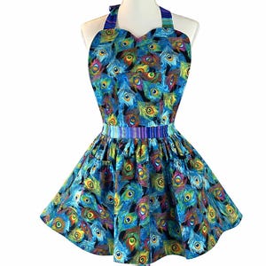 May include: A blue apron with a peacock feather pattern. The apron features a heart-shaped bodice and a flared skirt. The fabric is decorated with blue, green, yellow, and orange feather designs. The apron is displayed on a white mannequin.