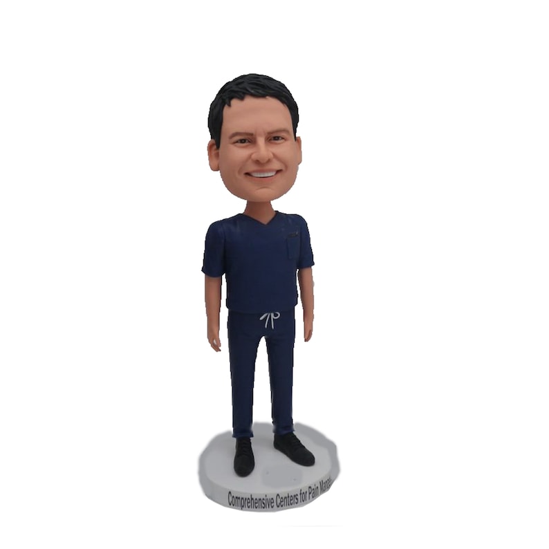 May include: A figurine of a person wearing blue scrubs, with a smiling face. The figurine is standing on a base with the text "Comprehensive Centres for Pain Management".