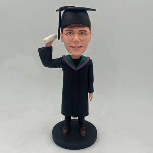 Figura cabezona de graduación personalizada. Levanta una mano hacia su diploma de graduación y anima su graduación.