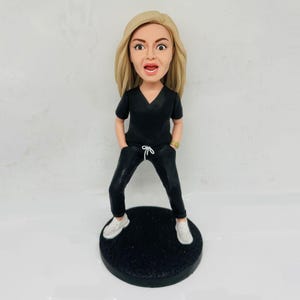Statuetta personalizzata di un'infermiera in camice nero, con orologio d'oro e scarpe bianche. Un regalo perfetto per il personale medico.