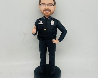 May include: A custom bobblehead figurine of a person wearing a black uniform with a badge and a gold star. The person is giving a thumbs up.