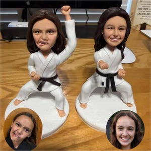 Może przedstawiać: Dwie niestandardowe figurki typu bobblehead przedstawiające osobę w karate, z czarnym pasem. Figurki stoją na białych podstawach, każda ze zdjęciem osoby. Jedna figurka ma uniesioną pięść, druga jest w pozycji karate.