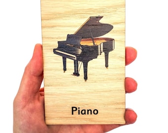 May include: A wooden card with a black and white image of a grand piano. The text "Piano" is printed below the image.
