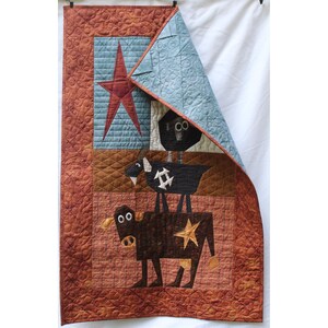 May include: A handmade quilt featuring a stacked animal design. The quilt showcases a brown cow, a black goat, and a black bird, each with star accents. The background includes a red star and a light blue section.