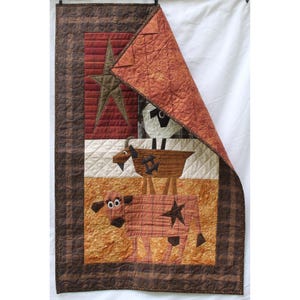 May include: A handmade quilt with a patchwork design. The quilt features a star and farm animals, including a sheep, goat, and cow. It has a brown border and a rust-coloured backing.