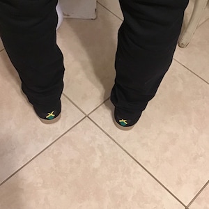 May include: A pair of black pants with a pair of shoes featuring the Jamaican flag on the back.