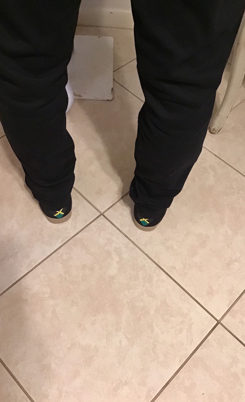 May include: A pair of black pants with a pair of shoes featuring the Jamaican flag on the back.