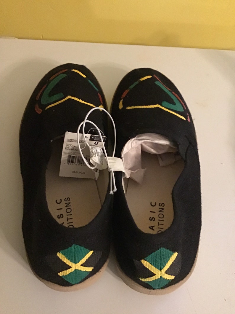 May include: A pair of black canvas slip-on shoes with a yellow, green, and black Jamaican flag design on the toe. The shoes have the text "ASIC  EDITIONS" on the side.