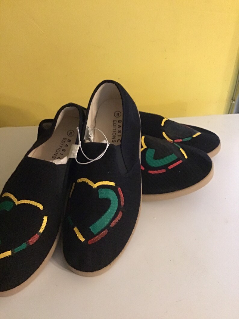 May include: Two pairs of black canvas slip-on shoes with a red, yellow, and green design. The shoes have the text "BASIC EDITIONS" on the side.