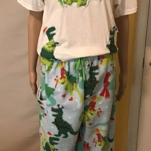 Puede incluir: Camiseta blanca con un dinosaurio verde que lleva un gorro de Pap&aacute; Noel y un &aacute;rbol de Navidad en la espalda. Pantal&oacute;n de pijama azul a juego con estampado de dinosaurio verde y &aacute;rboles de Navidad.