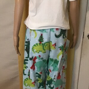 Puede incluir: Pantal&oacute;n de pijama azul con estampado de dinosaurio navide&ntilde;o. Los dinosaurios llevan gorros de Pap&aacute; Noel y bufandas. El pantal&oacute;n tiene un fondo blanco con lunares blancos.