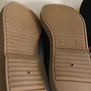 May include: Close-up of the soles of two brown canvas shoes with a textured pattern. The shoes have a white rubber trim around the edges.