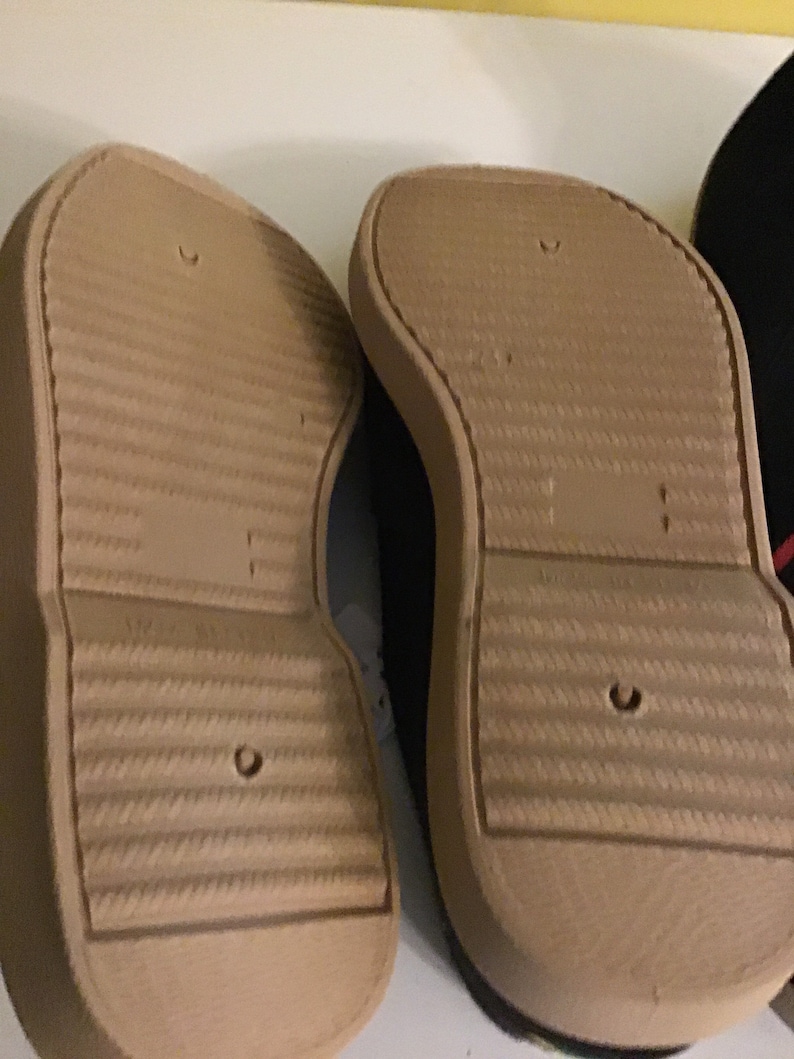 May include: Close-up of the soles of two brown canvas shoes with a textured pattern. The shoes have a white rubber trim around the edges.