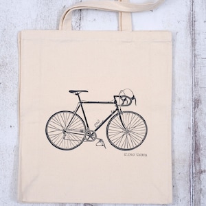 May include: A white canvas tote bag with a black silhouette of a bicycle printed on the front. The text "LINO LORD" is printed below the bicycle.