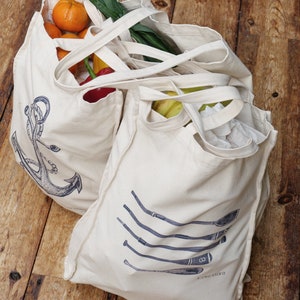 May include: Two white canvas tote bags with handles. One bag has a blue anchor design and the text "FIND YOUR" and the other bag has a blue design of five oars with the text "FIND YOUR" and a number 8.