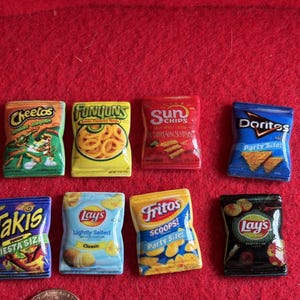 May include: A collection of eight miniature snack bag replicas featuring Cheetos, Funyuns, SunChips, Doritos, Takis, and three varieties of Lay's and Fritos. Each small, rectangular plastic item displays the brand logo, product name, and imagery.