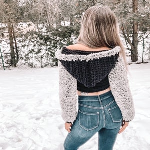May include: A black and white crocheted hooded crop top with a fluffy texture. The top has a loose fit and is cropped above the waist.