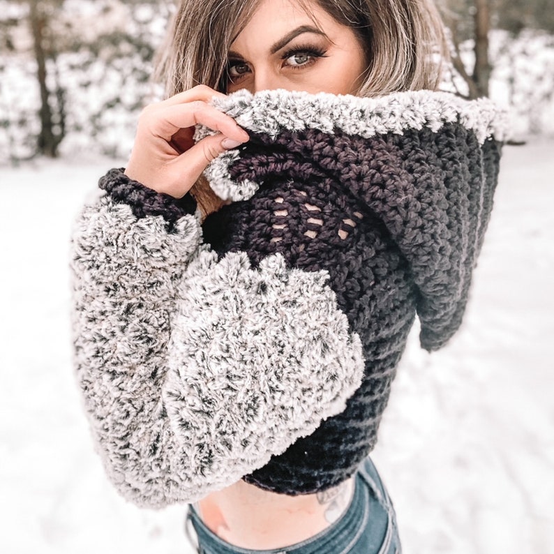 May include: A black and white crocheted hooded sweater with a fuzzy texture. The sweater is cropped and has a loose fit.