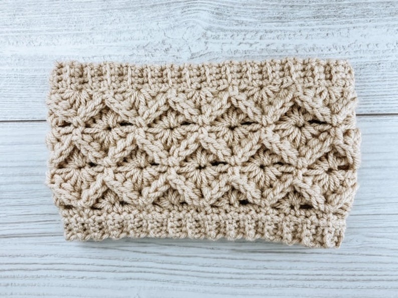 May include: A beige crocheted headband with a textured pattern. The headband is made with a single crochet stitch and has a simple, elegant design.