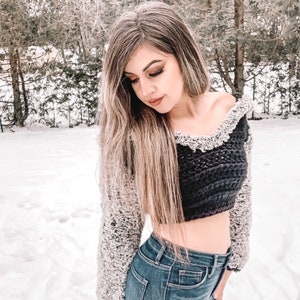 May include: A woman wearing a black and white cropped sweater with a fuzzy white trim. The sweater is worn over a pair of blue jeans.