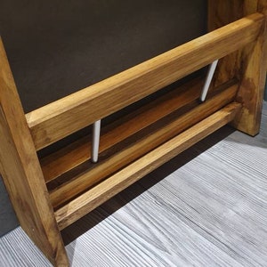 May include: Wooden wall-mounted shelf with two metal rods for hanging towels or other items. The shelf has a natural wood finish and is mounted on a white wall.
