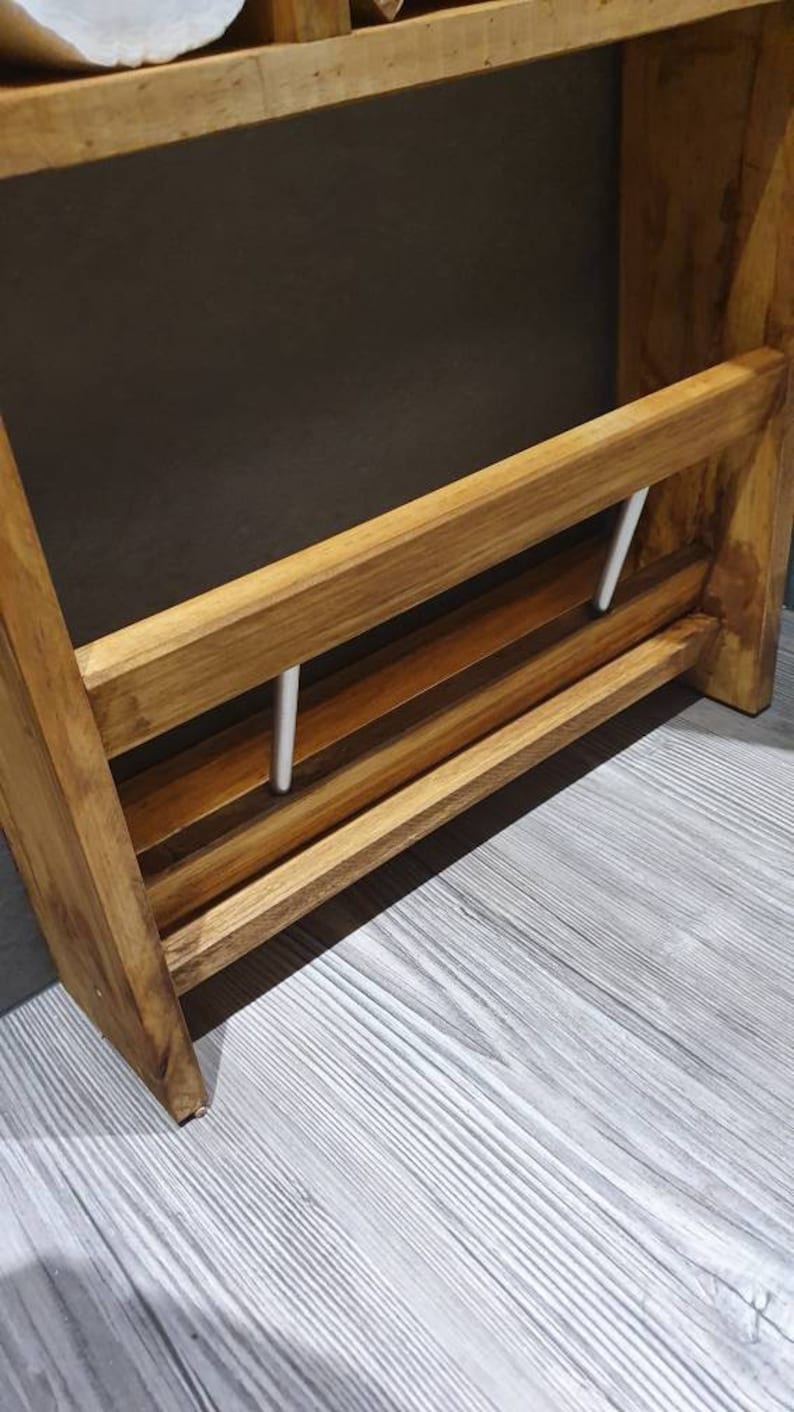 May include: Wooden wall-mounted shelf with two metal rods for hanging towels or other items. The shelf has a natural wood finish and is mounted on a white wall.