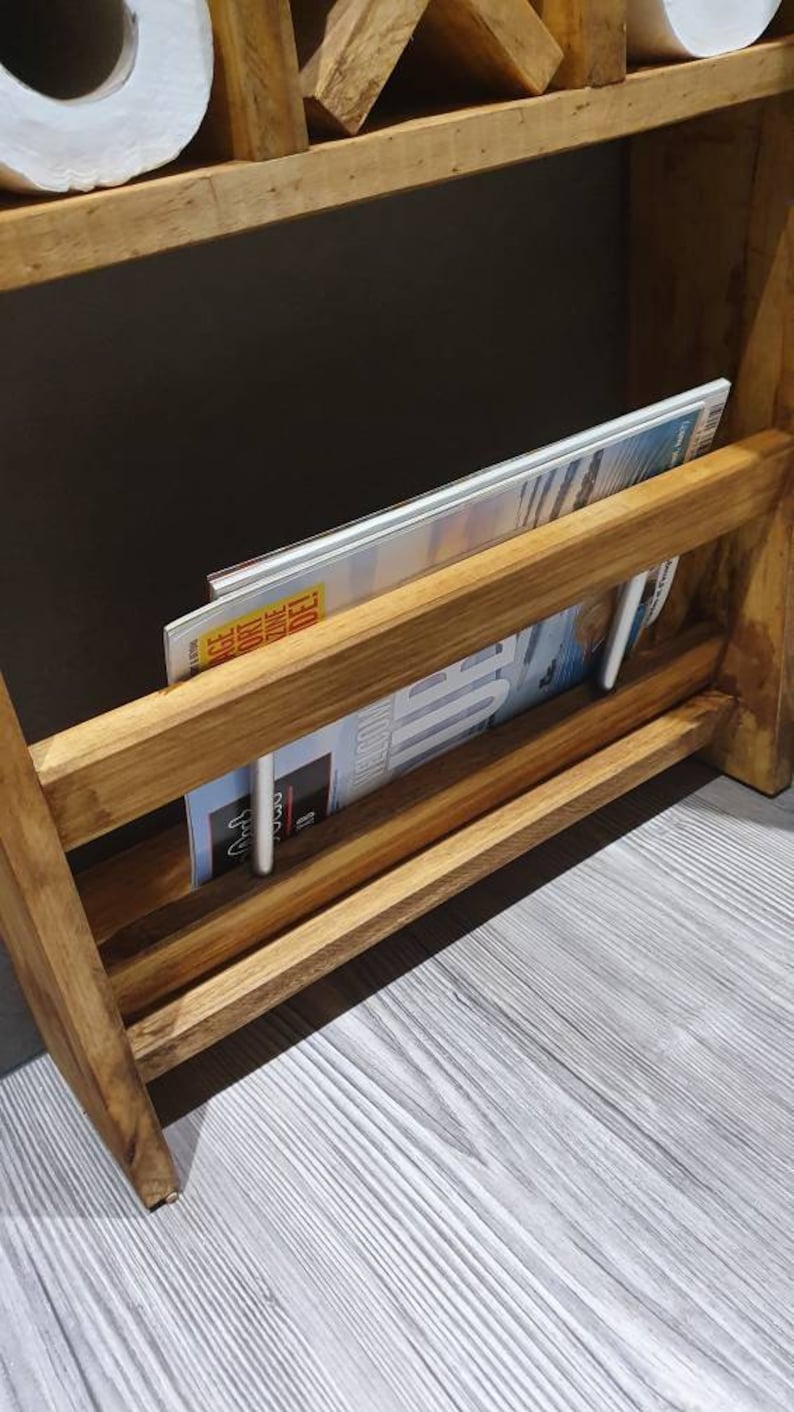 May include: A wooden shelf unit with two rolls of toilet paper and a magazine rack. The magazine rack has a magazine inside with the text "ACE" and "ONE DAY DELI".