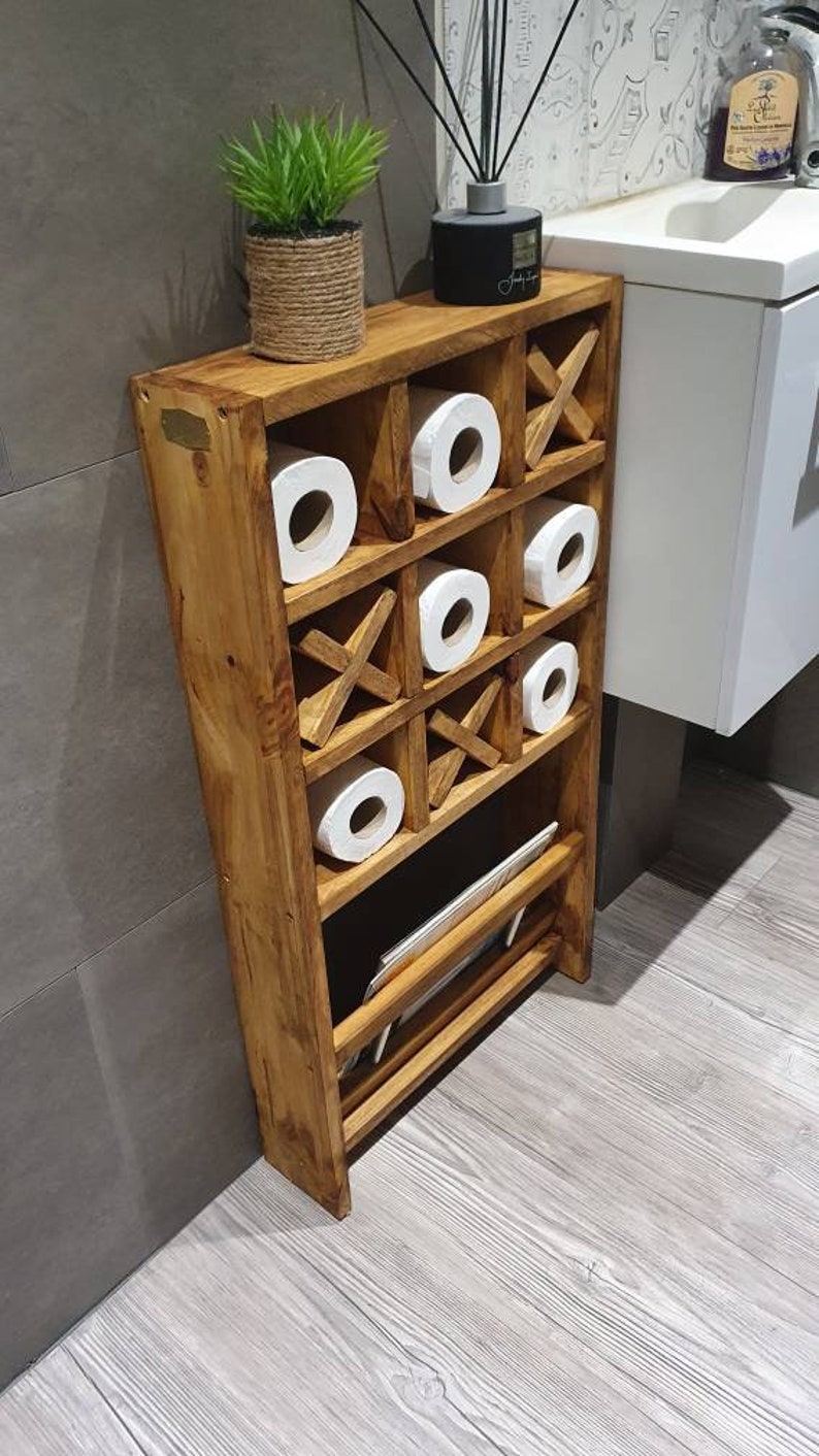 May include: A wooden bathroom storage shelf with a tic-tac-toe design. The shelf has six compartments for storing toilet paper rolls and a lower shelf for storing other items. The shelf is made of natural wood and has a rustic finish.