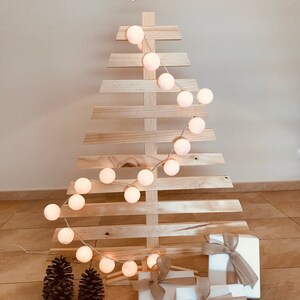 May include: A wooden Christmas tree with white cotton ball lights and wrapped gifts at the base.