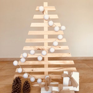 May include: A wooden Christmas tree decorated with white cotton ball lights and a white star on top. Three wrapped gifts with brown ribbon are at the base of the tree.