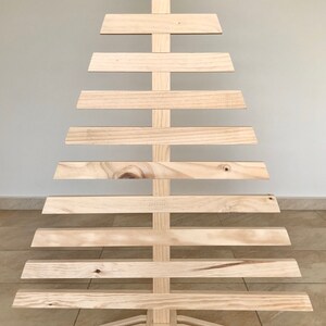 May include: A wooden Christmas tree made of 10 horizontal slats, with a triangular shape and a base with three legs.