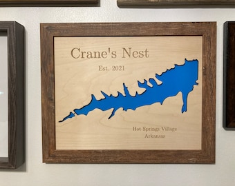 May include: A wooden framed wall art piece with a blue lake cutout and the text "Crane's Nest Est. 2021 Hot Springs Village Arkansas".