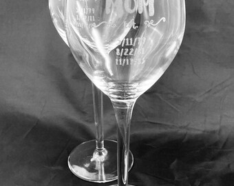 May include: Two clear glass wine glasses with etched designs. The glasses have the word "MOM" etched on them, along with the dates "7/11/79", "8/22/81", and "11/17/83".