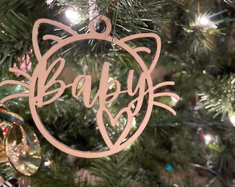 May include: A wooden Christmas ornament shaped like a cat's face with the word "Baby" written inside and a heart cutout.