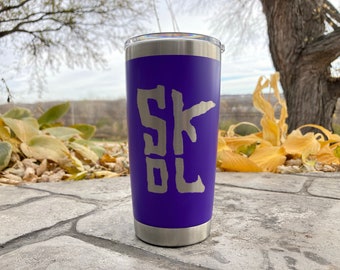 May include: A purple stainless steel tumbler with a silver inscription that reads "SKOL".