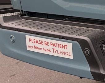 May include: A rectangular bumper sticker on a blue vehicle bumper. The sticker has red text that reads "PLEASE BE PATIENT my Mom took TYLENOL". The bumper is dusty and has a black top.