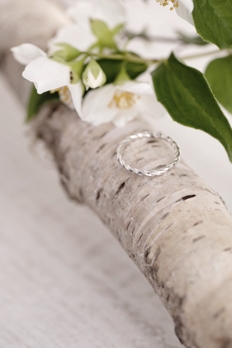 May include: A silver twisted ring on a piece of birch bark with white jasmine flowers.