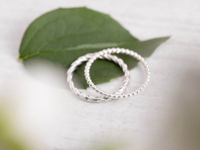 May include: Two silver rings, one with a twisted design and the other with a beaded design, are stacked on top of each other.