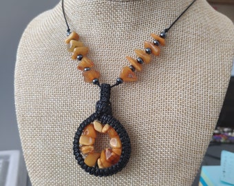 May include: A necklace with a round pendant made of black cord and amber stones. The pendant is surrounded by a circle of amber stones. The necklace is made of black cord and amber stones.