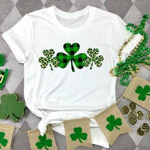 May include: White t-shirt with a green, black, and yellow shamrock design. The shamrock is made up of three individual shamrocks, one with a black and white plaid pattern, and two with a leopard print pattern.