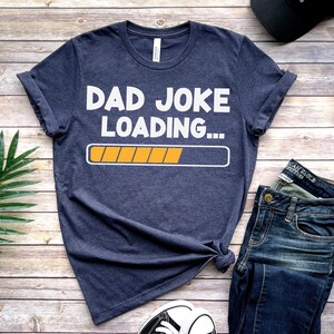 May include: A navy blue t-shirt with the text "Dad Joke Loading..." in white with a yellow progress bar.