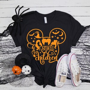 May include: Black t-shirt with a Mickey Mouse silhouette and the text "I smell children" in orange. The silhouette includes a witch's hat, bats, and stars.