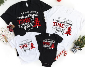 May include: Four black and white t-shirts with a red and black plaid Christmas tree design. The shirts have the text "It's the most wonderful time of the year" on them.