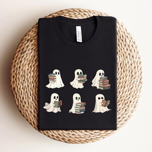Może przedstawiać: Czarny T-shirt z grafiką sześciu białych duch&oacute;w trzymających lub czytających książki. Duchy są w r&oacute;żnych pozach, niekt&oacute;re trzymają stosy książek, inne czytają jedną książkę.