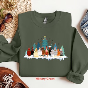 May include: A military green sweatshirt with a Christmas-themed design featuring a group of chickens in front of a decorated Christmas tree. The text "Military Green" is printed on the bottom of the sweatshirt.