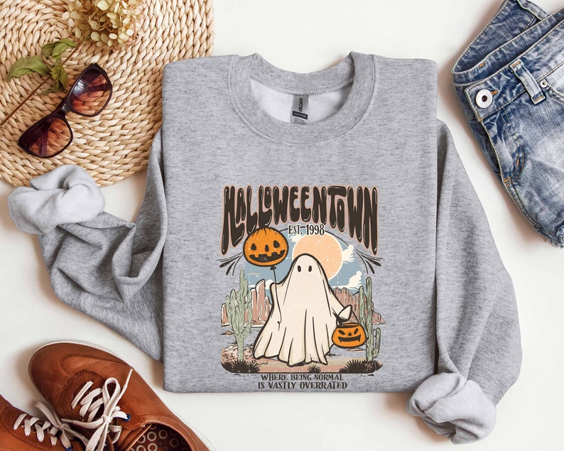 May include: Gray sweatshirt with a graphic print of a ghost holding a jack-o-lantern. The text on the graphic reads "Halloweentown Est. 1998" and "Where being normal is vastly overrated".